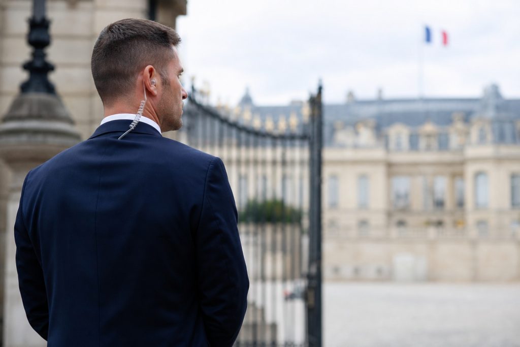 Agent de protection rapprochée en costume devant un bâtiment institutionnel parisien, illustrant le métier de garde du corps présidentiel.